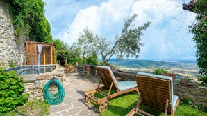 A stone patio with two wooden lounge chairs, a small pool, and a view of the countryside. - Stone house villa with Spa in Cortona (Cortona)