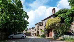 A cobblestone street in a historic village with stone buildings, a parked car, and lush greenery. - Stone house villa with Spa in Cortona (Cortona)