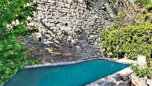 A swimming pool with a stone wall and greenery around it. - Stone house villa with Spa in Cortona (Cortona)