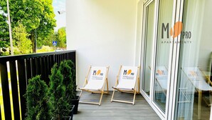 Een balkon met plantenpotten, twee schildersezel met promotieposters en een glazen deur met een logo.