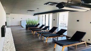 Een moderne spa met houten vloer, zwarte loungestoelen en een groot raam met uitzicht op het omliggende landschap.