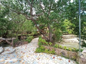 Um caminho de azulejos serpenteia por um jardim exuberante, com uma ponte e uma estrutura de pedra.