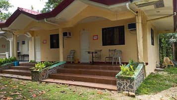 A two-story building with a covered porch, a dining area with a table and chairs, and a small garden area with steps leading to the entrance.