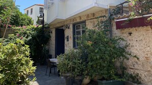 A two-story house with white walls and a tiled roof. There are potted plants and a table outside.