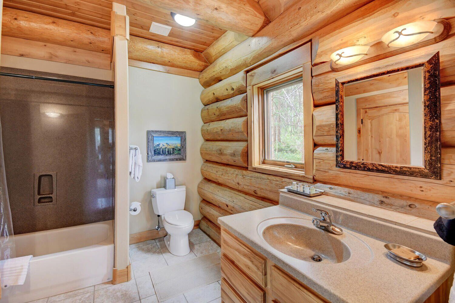 A log cabin bathroom with a shower, toilet, sink, and a large mirror.