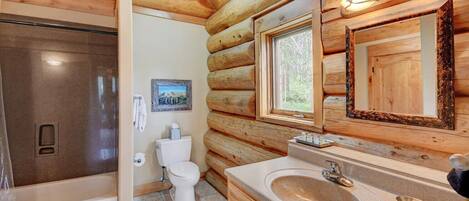 A log cabin bathroom with a shower, toilet, sink, and a large mirror.