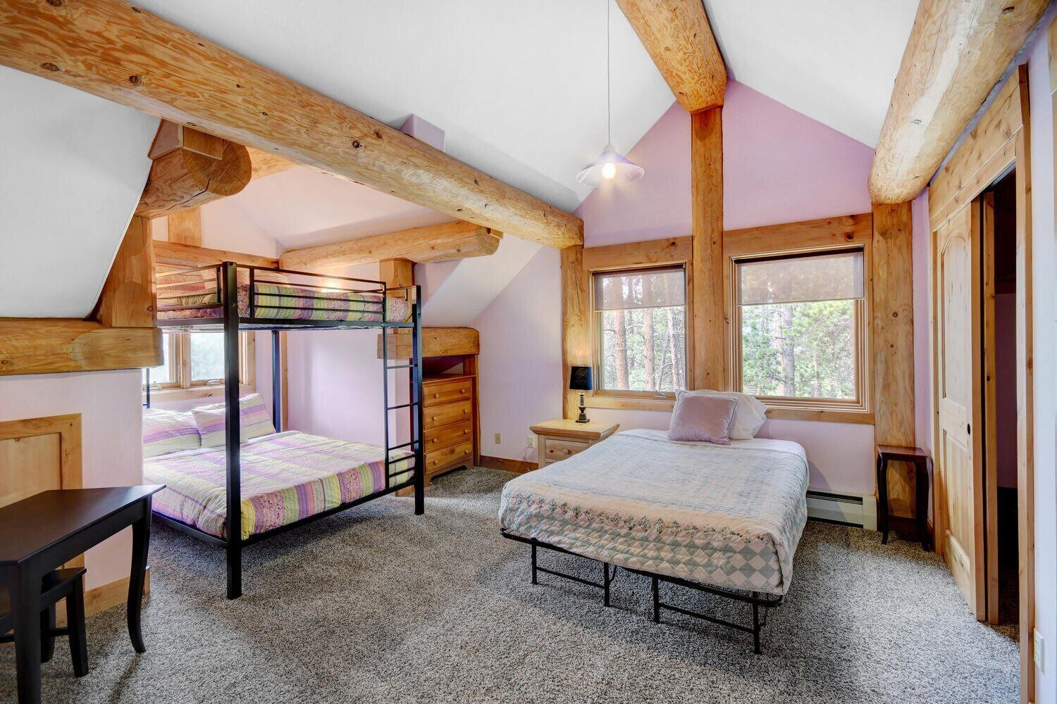 Een gezellige slaapkamer met een stapelbed, een enkel bed en een dressoir. Er zijn ramen die natuurlijk licht en uitzicht op bomen bieden.
