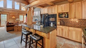 A spacious kitchen with wooden cabinets, a central island, and a stone fireplace. - Mountain View Log Home I Hot Tub I Arcades I Great Views I Sauna I Discounted Attractions (Fraser)