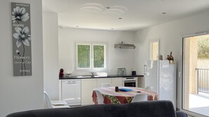 Een moderne keuken met witte kasten, een eettafel met een bloemrijk tafelkleed en een grijze bank op de voorgrond.