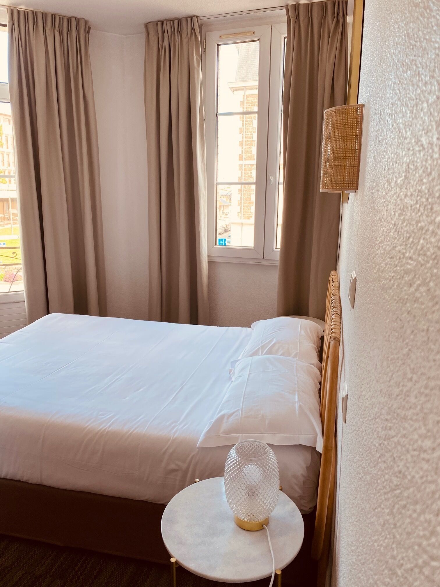 A hotel room with a bed, a round table with a lamp, and a window with curtains.