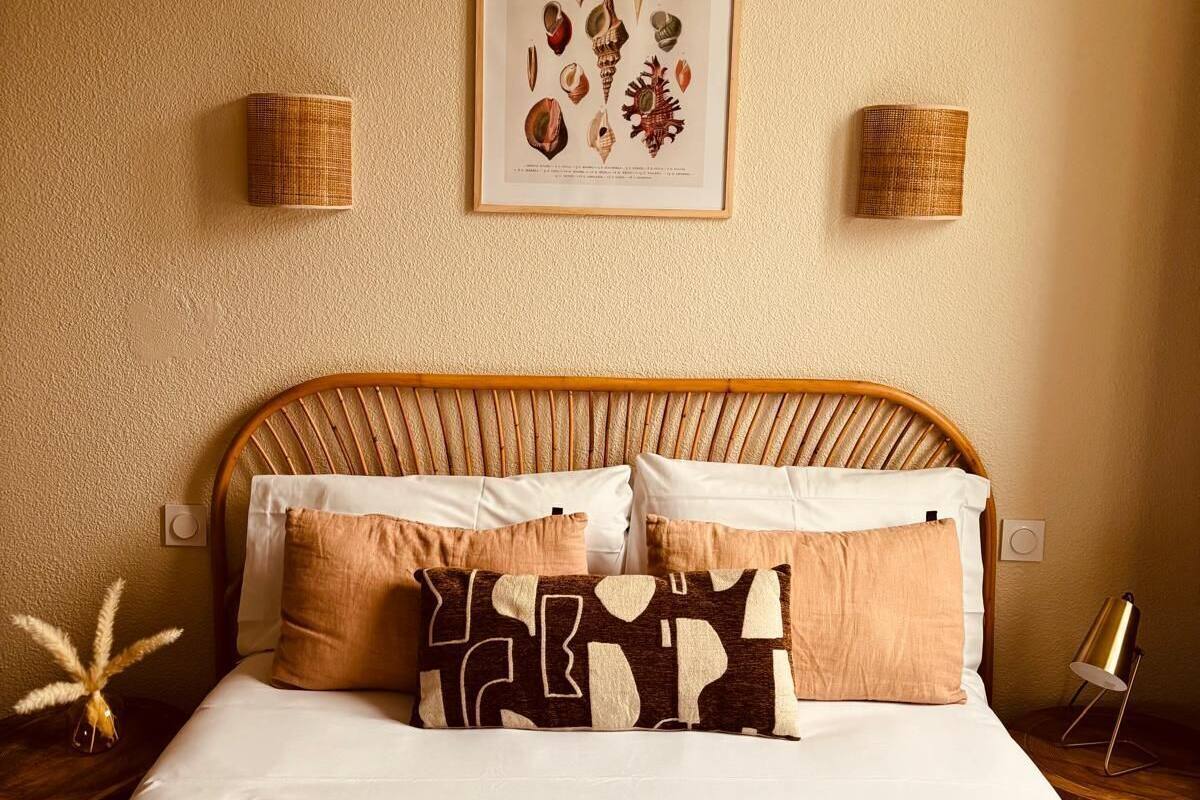 A bedroom with a bed, pillows, a headboard, a framed picture on the wall, and two wall-mounted lamps.