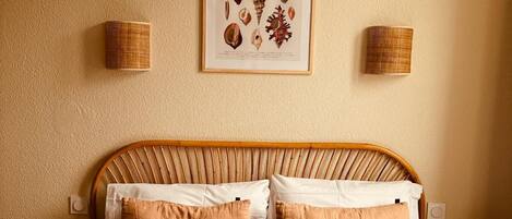 Une chambre à coucher comprenant un lit, des oreillers, une tête de lit, un tableau encadré accroché au mur et deux lampes fixées au mur.