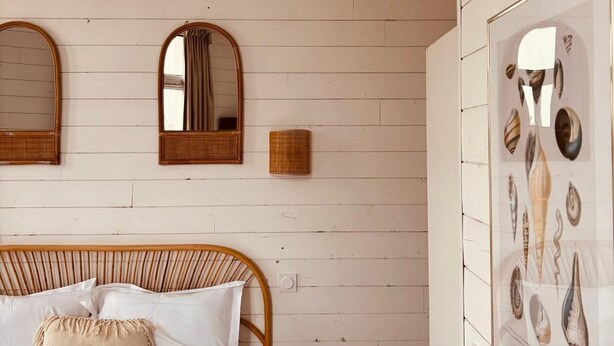 A bedroom with a bed, two wall-mounted mirrors, a wall-mounted light fixture, and a framed seashell artwork. - Hôtel Le Britannic (Saint-Malo)