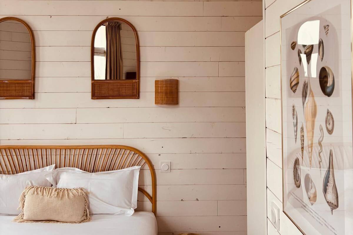 A bedroom with a bed, two wall-mounted mirrors, a wall-mounted light fixture, and a framed seashell artwork.