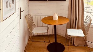 A corner room with a round wooden table, two wireframe chairs, a mounted flat-screen TV, and a framed seashell artwork on the wall. - Hôtel Le Britannic (Saint-Malo)