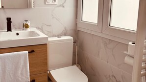 A bathroom with a marble wall, a white sink, a toilet, and a towel rack. - Hôtel Le Britannic (Saint-Malo)