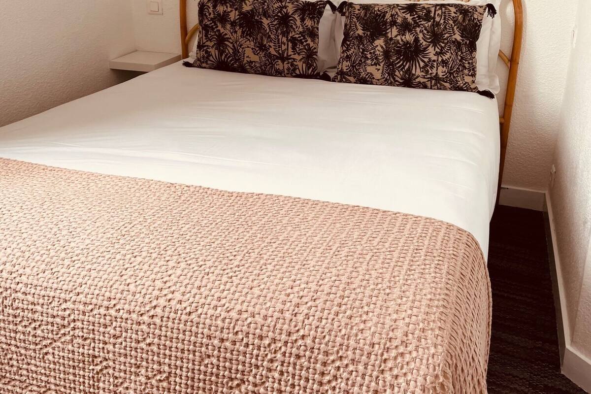 A neatly made bed with a woven blanket, a wooden headboard, and two wall-mounted light fixtures.