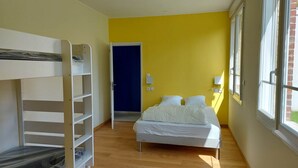 Ein Zimmer mit Etagenbett, Einzelbett, Tür und Fenster.