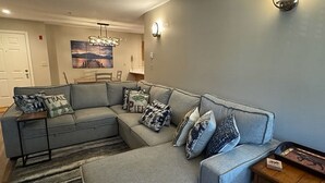 Een woonkamer met een grijze modulaire bank, een vloerkleed en een schilderij aan de muur.