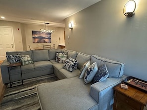 A living room with a grey sectional sofa, a rug, and a painting on the wall.