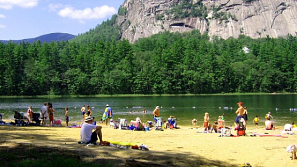 A beach with people sunbathing and swimming, surrounded by dense forest and a large rock formation. - Perfect vacation getaway. #237 (Lincoln)
