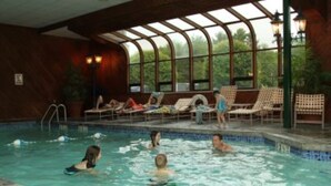 An indoor swimming pool with clear glass walls, lounge chairs, and a view of greenery outside. - Perfect vacation getaway. #237 (Lincoln)