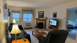 A living room with a sofa, armchair, coffee table, lamp, fireplace, television, and a door leading to another room. - Perfect vacation getaway. #237 (Lincoln)