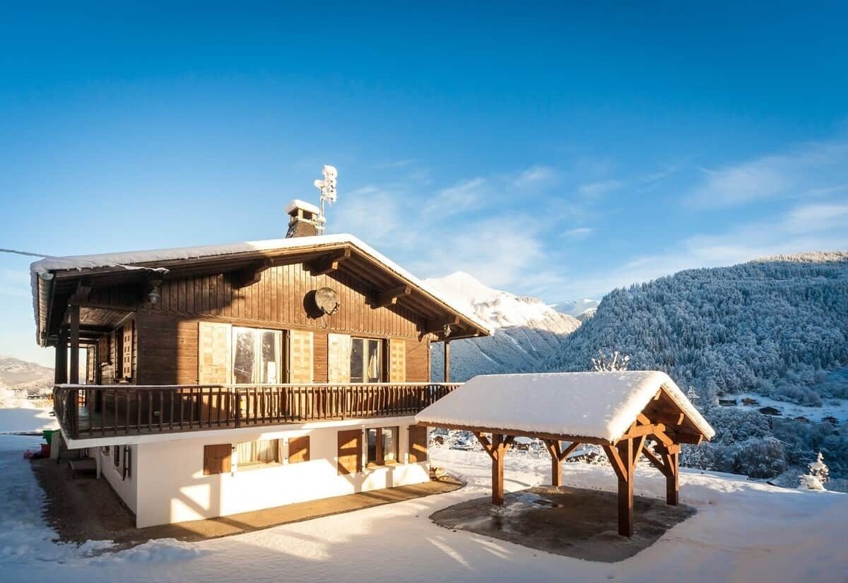 Un chalet en bois doté d’un balcon, d’un espace extérieur aménagé et abrité, et surplombant un paysage montagneux enneigé.