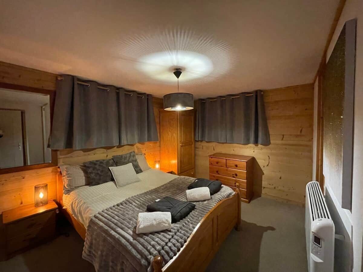Ein gemütlicher Holzraum mit Bett, Nachttischen, einem Schminktisch und einer Deckenleuchte.