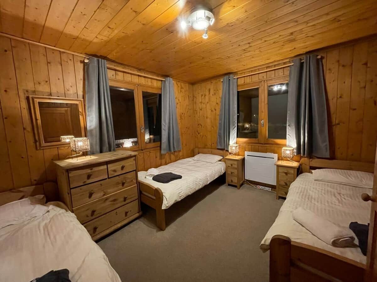 A wooden-paneled room with two beds, a dresser, a mirror, and a window with curtains.