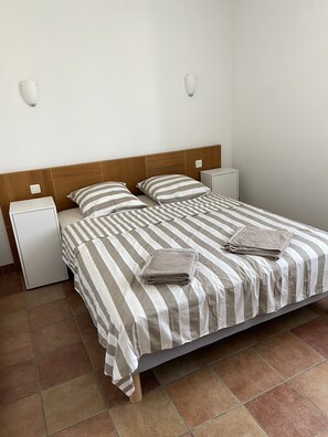 Cama bem arrumada com roupa de cama listrada, uma pequena mesa de cabeceira e um criado-mudo.
