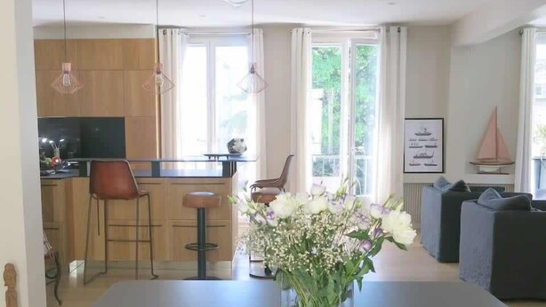 A modern dining area with a long table, a vase of flowers, and a kitchen in the background. - Sacré Coeur CityCosy (Paris)
