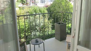 A balcony with a table and a potted plant, overlooking a garden and neighboring buildings. - Sacré Coeur CityCosy (Paris)