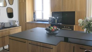 A modern kitchen with wooden cabinets, a central island with a fruit bowl, a black countertop, and a pendant light. - Sacré Coeur CityCosy (Paris)