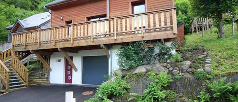 A wooden cabin with a balcony, a garage, and a stone retaining wall.