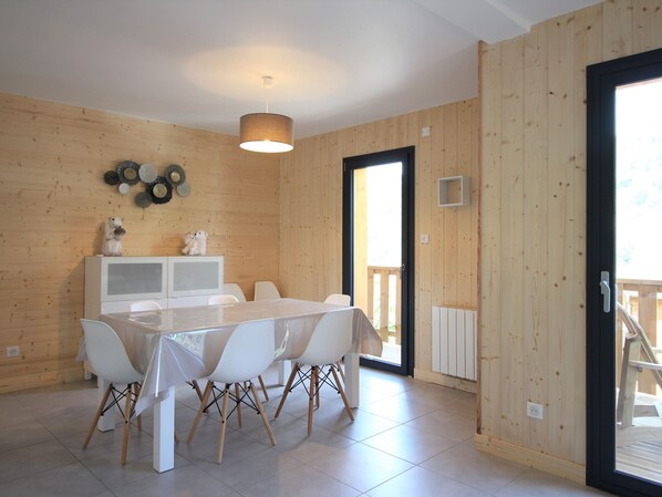 A modern kitchen with white cabinets, a dining table with chairs, and a hanging light fixture. - Modern chalet 92m², Wi-Fi, near Mont-Dore (Mont-Dore)