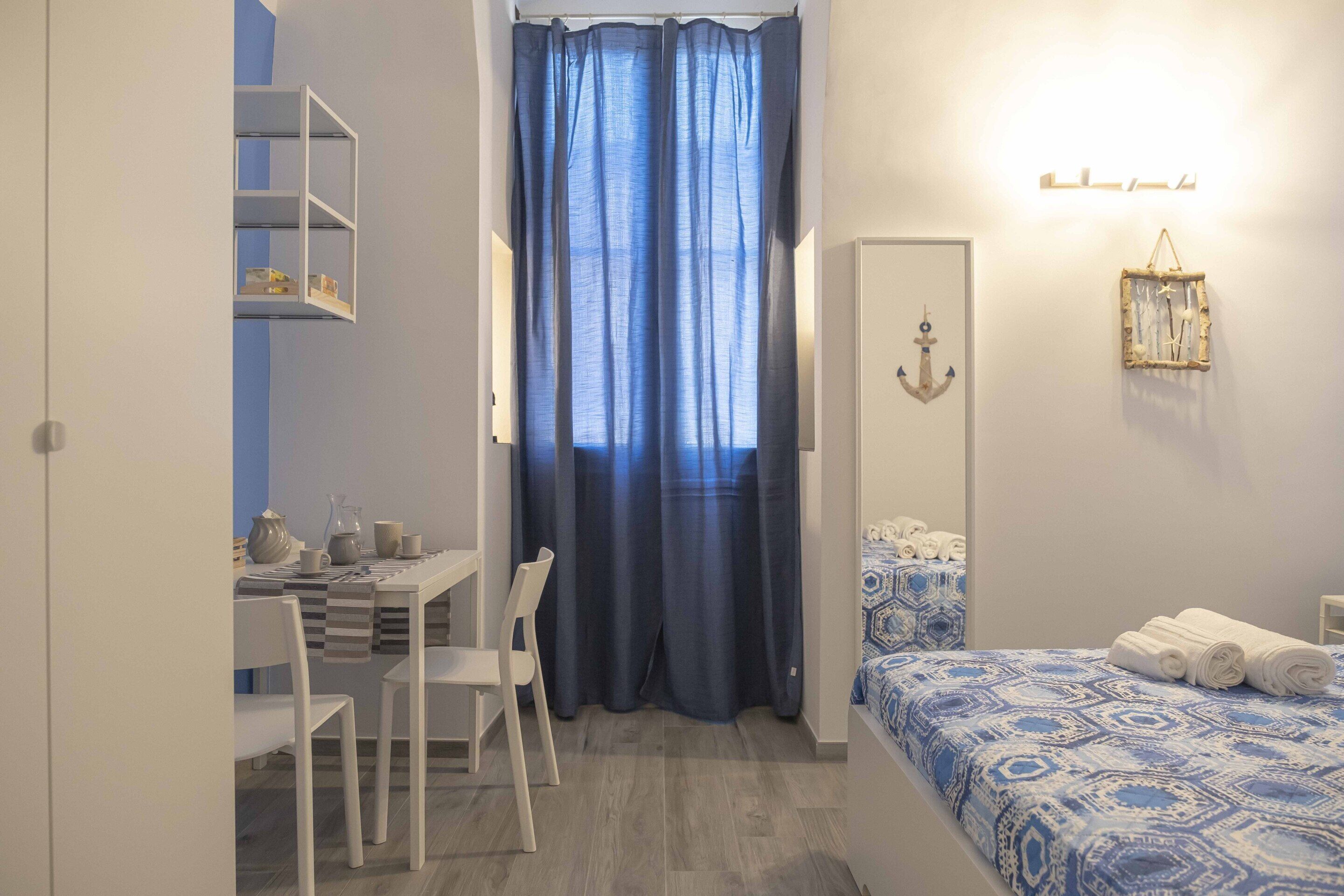 A room with a bed, a desk, chairs, a curtain, and a wall-mounted light fixture.