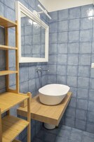 Un baño con un lavamanos blanco, estantes de madera y azulejos azules.