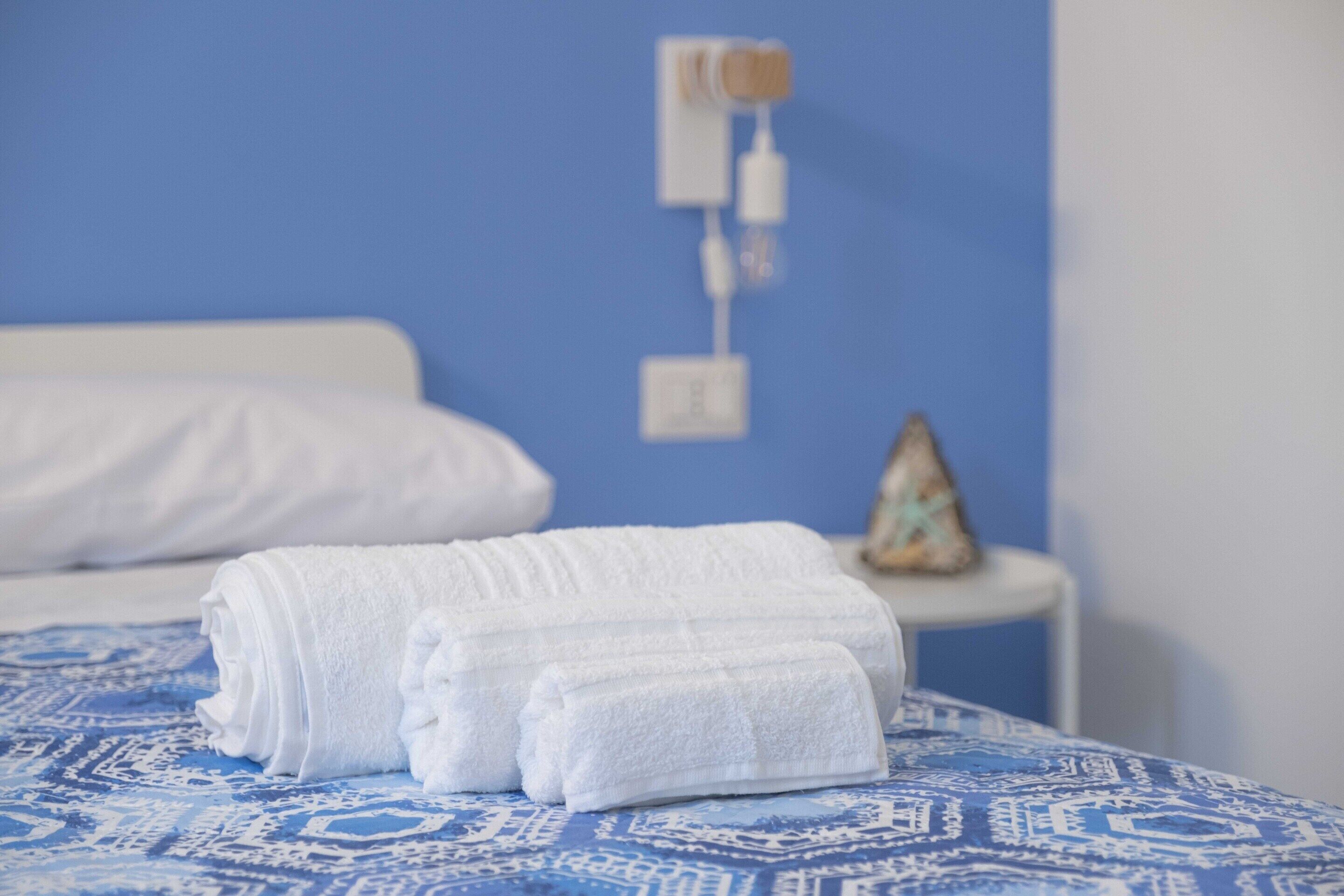 Ein ordentlich bezogenes Bett mit weißen Handtüchern, einer blauen Tagesdecke mit Muster und einem kleinen Nachttisch mit einer Dekoration.