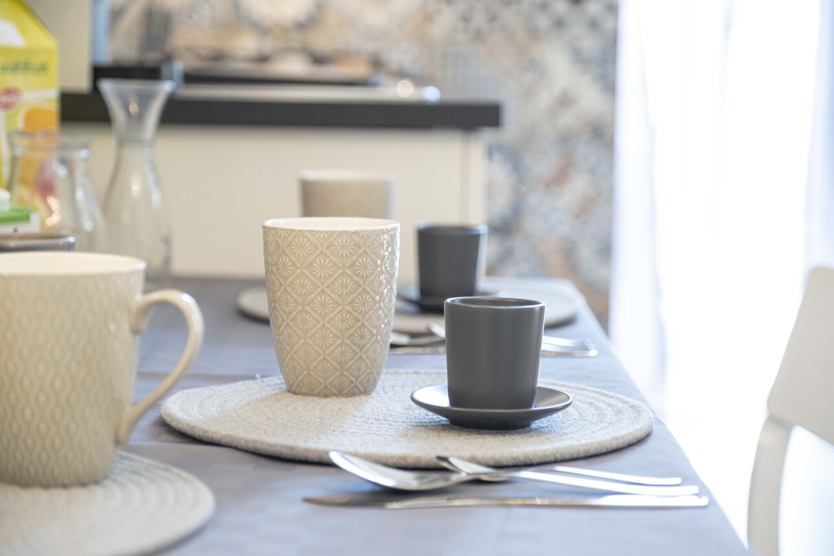 Una mesa de comedor con una taza blanca, una taza estampada y una taza oscura sobre individuales.
