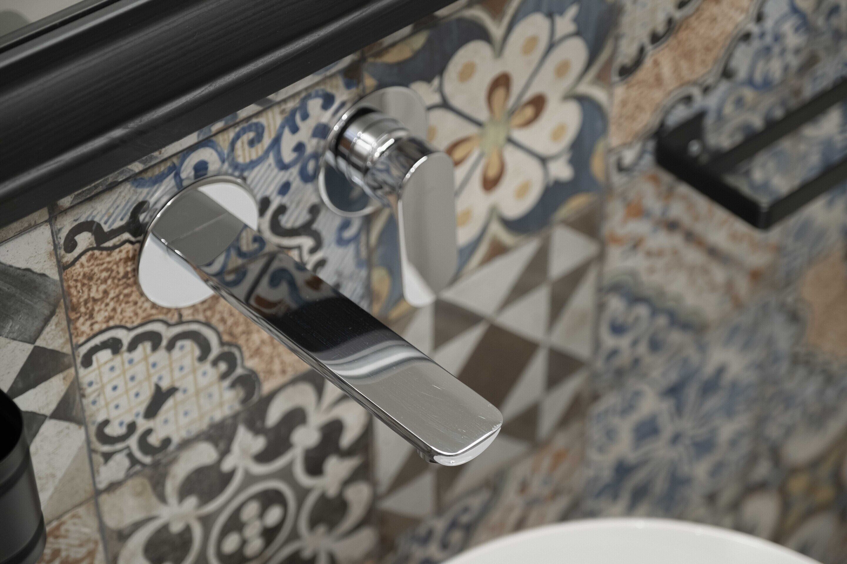 A bathroom with a tiled wall featuring a floral pattern and a chrome faucet.