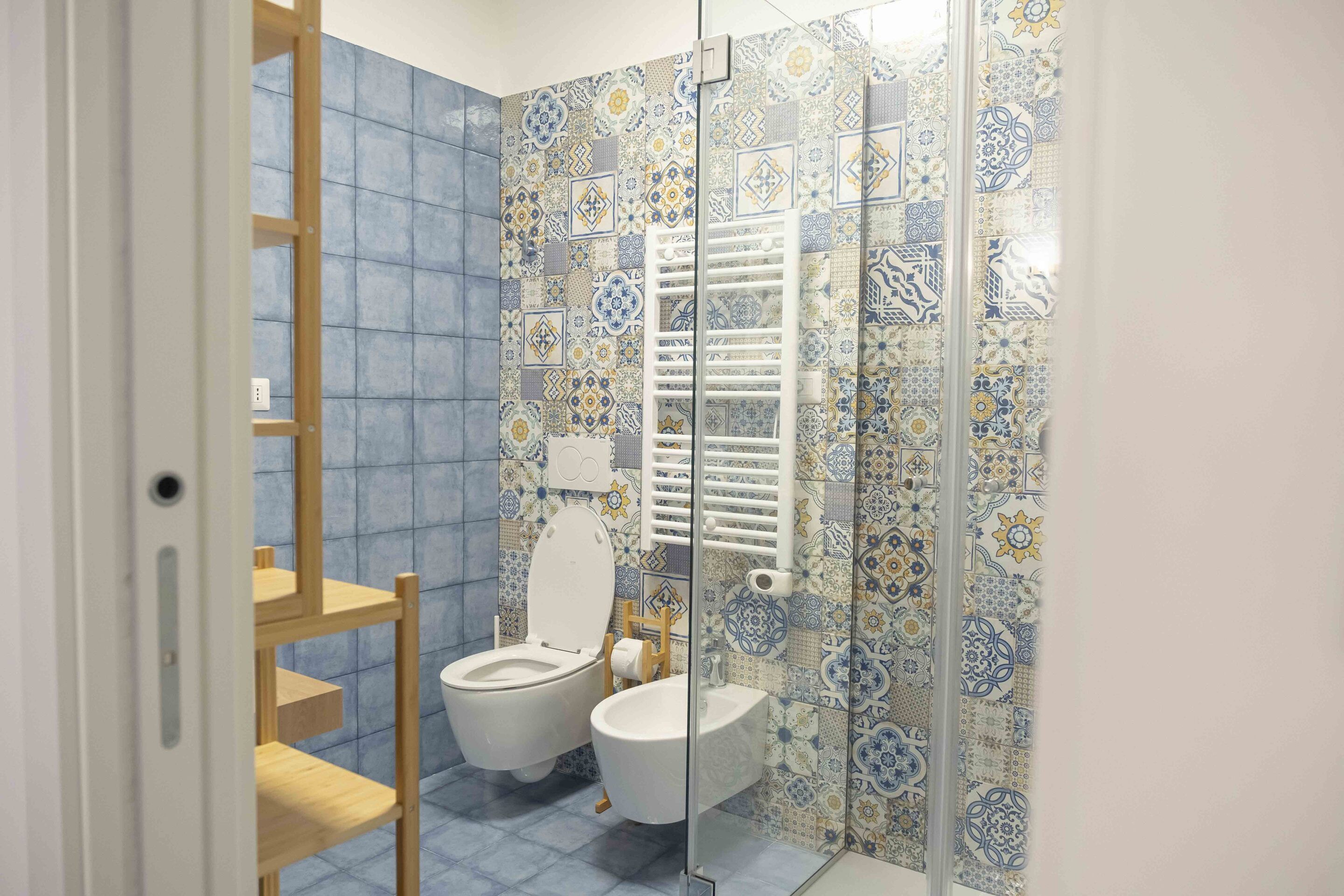 A bathroom with a blue tiled wall, a white toilet, a white sink, and a glass shower enclosure.