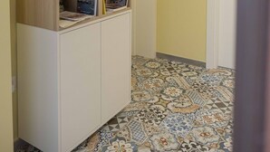 A hallway with a wooden cabinet displaying books, a framed map on the wall, and patterned floor tiles. - Il Pendio B&B (Bisceglie)