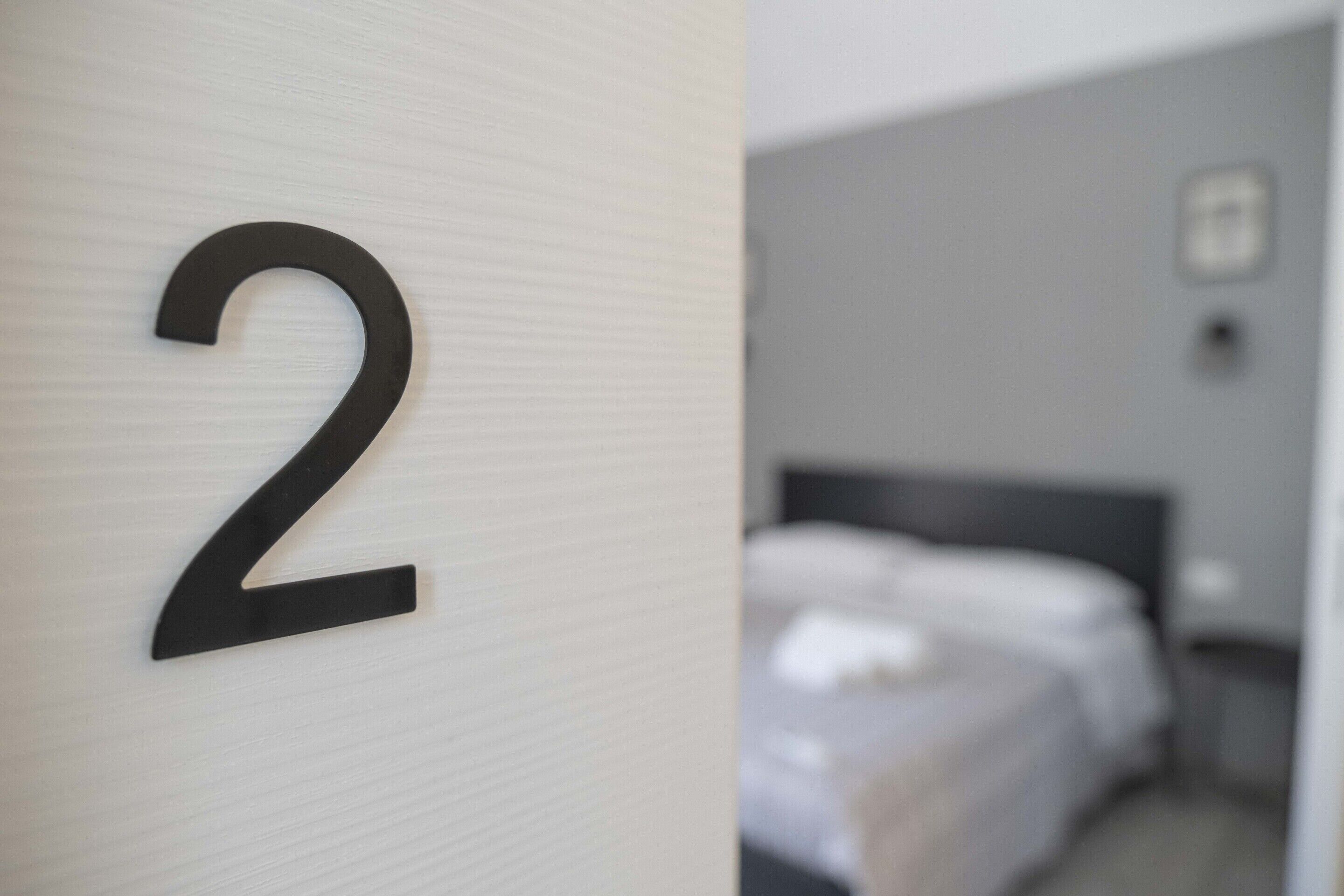 A hotel room with a large number '2' on the wall, a bed, a nightstand, and a picture on the wall.