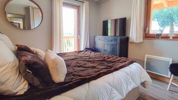 A bedroom with a bed, a television, a dresser, and a window with curtains.