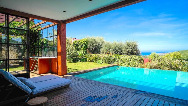 A wooden deck with a pool, outdoor seating, and a view of the sea.
