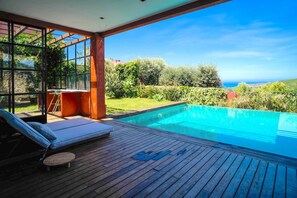 A wooden deck with a pool, outdoor seating, and a view of the sea.