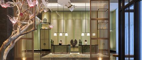 A lobby with a reception desk, a decorative tree, and a large window.