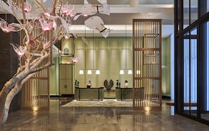 A lobby with a reception desk, a decorative tree, and a large window. - Shangri-La Qiantan, Shanghai (Shanghai)
