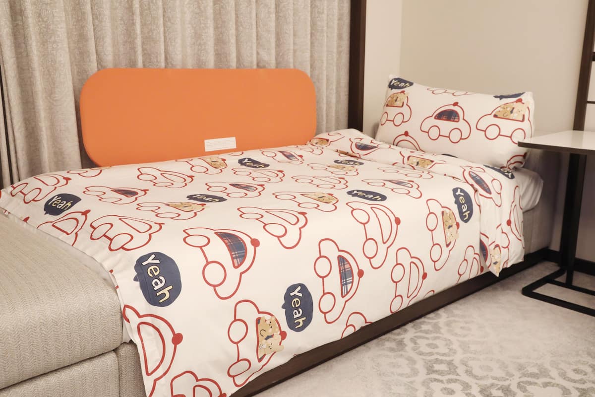 A hotel room with a bed featuring a patterned bedspread, an orange headboard, and a matching pillow.